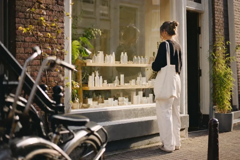 Vrouw blijft staan voor de etalage van een kleine skincarewinkel in een zonnige Amsterdamse straat